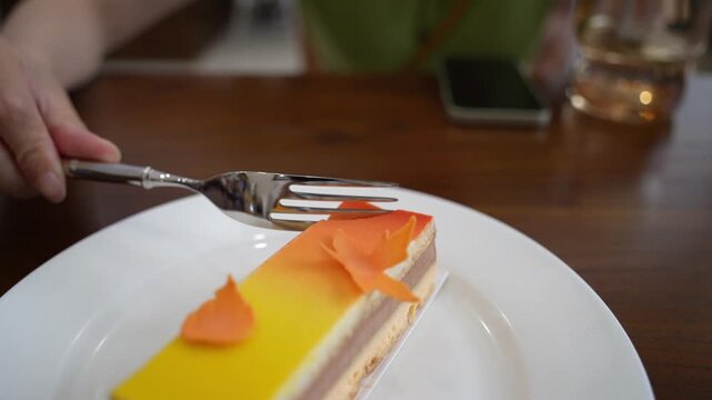 Eating pomelo mousse cake on wooden table, by using a silver fork