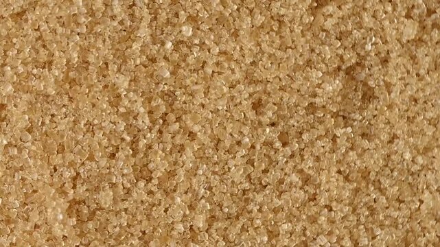A high-angle, macro shot showcasing a detailed texture of unrefined brown cane sugar crystals. The slow, smooth camera movement captures the shimmering surface and natural golden-brown color of the pr