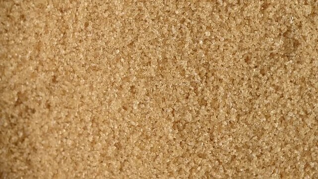 A high-angle, macro shot showcasing a detailed texture of unrefined brown cane sugar crystals. The slow, smooth camera movement captures the shimmering surface and natural golden-brown color of the pr