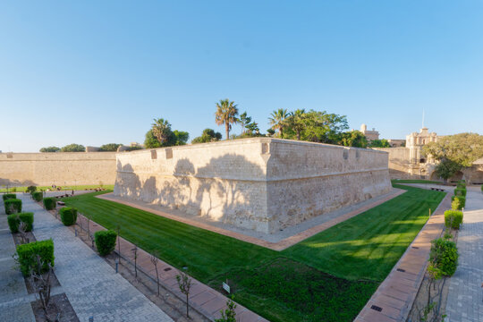 Historic stone bastions and defensive limestone walls with green lawns and palm trees in Mdina, Malta