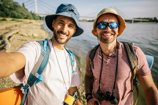 Gay male couple taking selfie while hiking by river trail