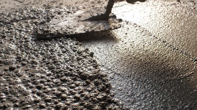Fresh cement being spread with a trowel, close-up view of construction work, wet concrete texture
