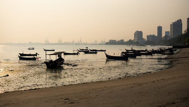 Traditional fishing boats anchored along a coastal shoreline at low tide with a distant city skyline, capturing a peaceful maritime scene and urban waterfront landscape