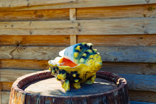 Ai dreptate, scuze! Iată corectat:
Title: Colorful Painted Decorative Seashell with Yellow Blue and Orange Colors Displayed on Wooden Barrel Against Rustic Plank Wall in Garden