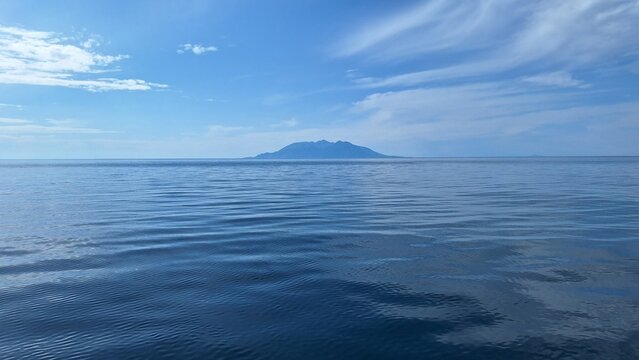 Calm Aegean Sea waters with the distant silhouette of Samothrace Island viewed from G&ouml;k&ccedil;eada, Turkey, beneath a serene blue sky.