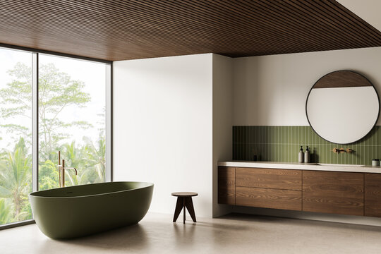 Minimalist bathroom interior with green freestanding tub, wood cabinetry and large window overlooking lush trees in serene style. 3D Rendering