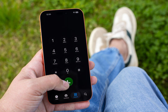 Man hand holding Phone Apple iPhone 17 Pro Max Cosmic Orange outdoor, displaying phone dialer keypad with numbers and green call button on the screen IOS 26