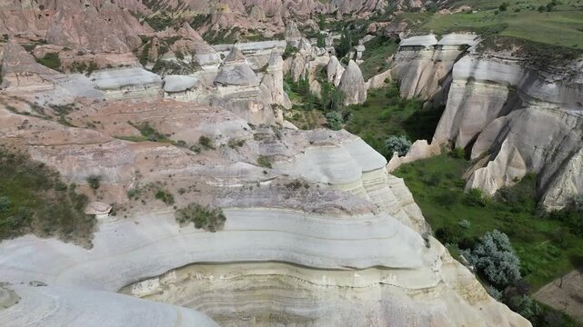 Smooth 4K drone footage flies low over Red Valley, Cappadocia, revealing rounded volcanic hills and tall tufa columns with grey stone caps unique geological formations shaped by centuries of erosion