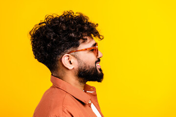Smiling young man profile portrait with curly hair, beard and glasses against vibrant yellow background in casual shirt — studio lifestyle portrait conveying confidence and positive mood © deagreez
