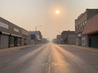 Fototapeta premium Empty desolate street in a small town during a hazy sunrise, evoking an eerie, abandoned atmosphere