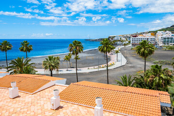 Fototapeta premium Elevated view of a coastal resort beach with black sand, palm trees, and terracotta roofs in Puerto Naos, La Palma, Canary Islands, Spain