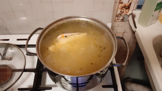 Chicken broth cooking in stainless steel pot on gas stove