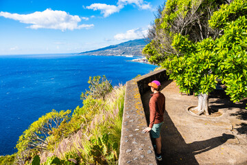 Naklejka premium Female tourist stands at a walled viewpoint looking at the blue coast, La Palma, Canary Islands, Spain