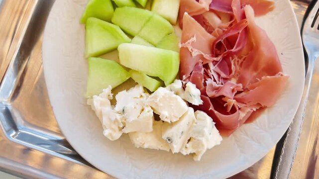 Top down view of plate with fresh green melon cubes, cured Spanish jamon slices, and blue cheese pieces served on a metal tray, Mediterranean appetizer