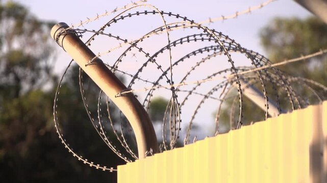 Close up handheld pan along razor wire security barrier with shallow depth of field