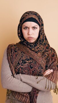 Young islamic woman wearing a traditional headscarf frowning and crossing her arms with a displeased and resentful facial expression. Vertical