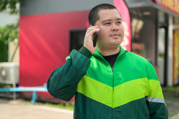 Plus size Thai delivery worker talking on smartphone outdoors near street landscape portrait © Ranta Images
