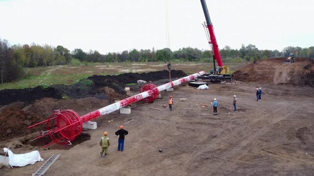 Aerial view of construction workers beside a red drilling rig and pipe section