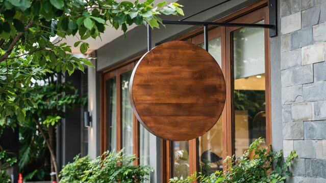 Blank round wooden hanging sign mockup on a shop facade with green foliage