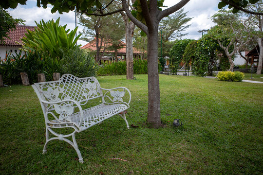 A white vintage metal benche in the green garden park