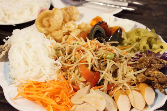 Famous Thai street food Som Tum Thad (papaya salad) with various side dishes and rice noodles