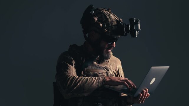 Soldier in tactical gear operates laptop with focused expression, showcasing advanced technology in a low-light environment, emphasizing military readiness and technical skills