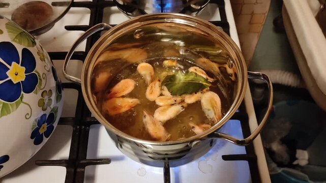Cooking shrimp with bay leaf in stainless steel pot on gas stove, top view