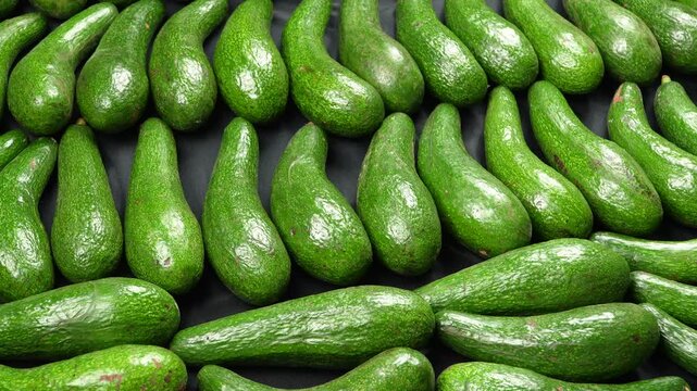 Macro zoom view of raw fresh long green avocados on dark background pattern.
