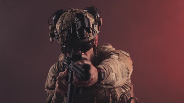 Military soldier in tactical gear aims firearm directly at the camera, showcasing intense focus and readiness in a dramatic lighting environment