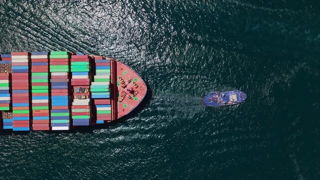 Aerial top-down view of a massive container ship loaded with colorful freight containers being escorted by a tugboat across the open sea, symbolizing global trade and maritime logistics