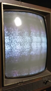 Vintage cathode ray tube television set displaying static noise on curved glass screen in dimly lit room