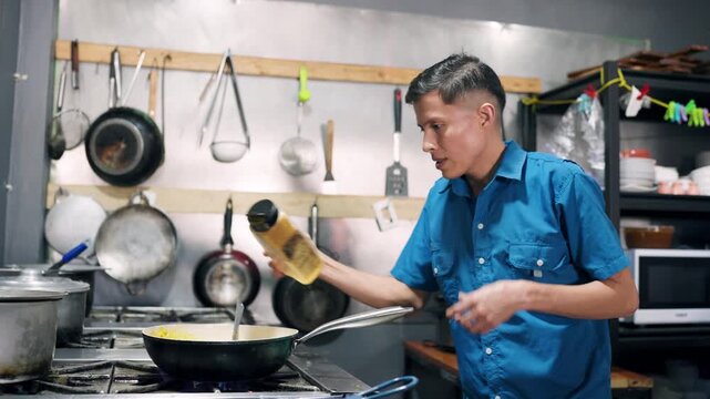 Young male chef skillfully adding spices to a dish cooking in a pan on a gas stove. Professional culinary setting in a Costa Rican restaurant
