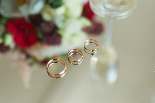 Macro shot of three golden wedding rings reflecting on mirror surface with bokeh.