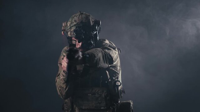 Soldier in tactical gear aims firearm directly at the camera, showcasing focused stance and intense expression in a smoky, dimly lit environment