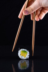 Chopsticks holding maki roll on black background © Aliaksandr