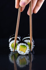 Hand picking cucumber maki roll on dark background © Aliaksandr