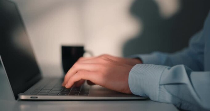 Business person typing fast on silver laptop keyboard during morning remote office work task.