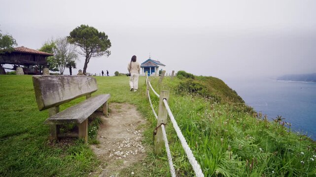 Woman with camera walking on coastal path at the Ermita de Santa Maria de Riegala