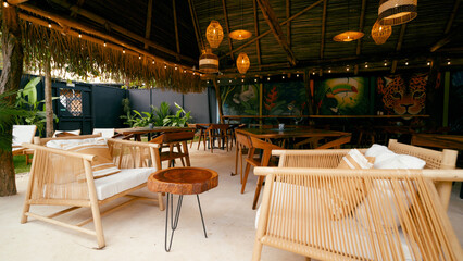 Fototapeta premium Inviting tropical restaurant showing natural bamboo furniture, wooden tables, thatched roof, and vibrant jungle animal murals