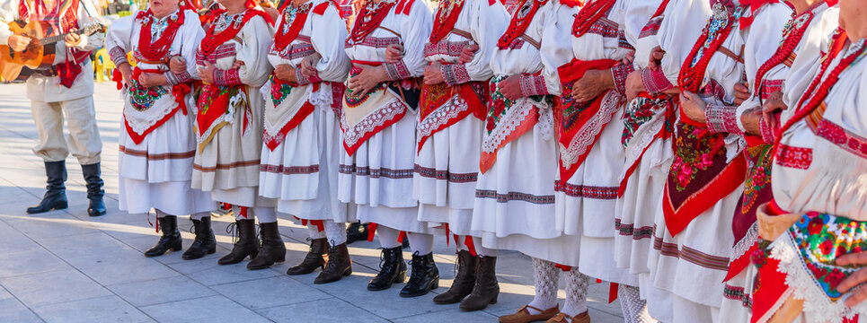 Close-up view of traditional Croatian folk attire featuring embroidered fabrics, lace details, accessories, and red bead necklaces during a cultural festival
