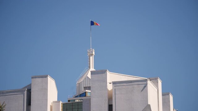 National flag of Moldova waving on a tall flagpole above a government building against a clear blue sky
