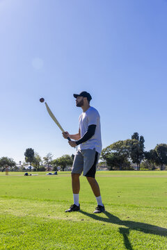 Cricket bat is being held in batting stance on grassy sports field near stumps, ball hovering