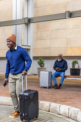 African American adult and senior men walking and sitting at terminal pulling suitcases, copy space © wavebreak3