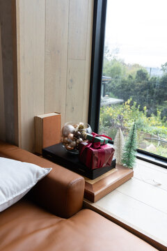 Tan leather sofa, white pillow flanking windowsill showing stacked platforms, glass bowl, red gift