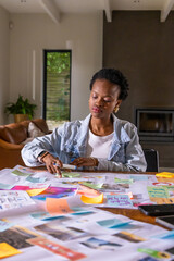 Obraz premium African American woman in denim jacket arranging sticky notes, pictures and papers at home