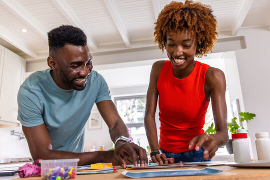 African American couple leaning and arranging colorful push pins and papers in bright kitchen