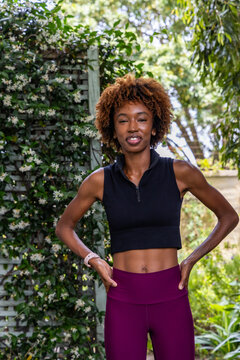 African American woman in 20s posing in garden trellis wearing crop top leggings showing smartwatch