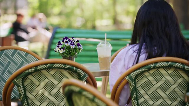 Iced coffee served on an outdoor cafe table surrounded by flowers and blurred visitors in a green park setting