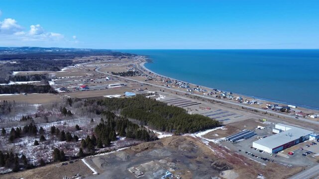 Elevated drone perspective of Quebec's iconic coastal highway, Route 132, passing through Matane beside the vast St. Lawrence River.
