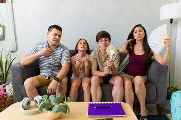 Family experiencing extreme heat indoors, cooling off using fans and looking uncomfortable during summer climate change